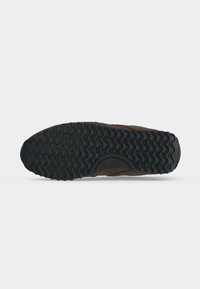 Semelle de chaussure en caoutchouc noir avec un motif ondulé et la taille 37 marquée près du centre sur fond blanc.