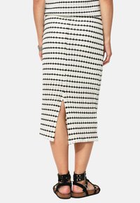 Jupe midi en tricot avec un motif rayé noir et blanc, dotée d'une fente au dos et d'une silhouette ajustée. Associée à des sandales à lanières noires.