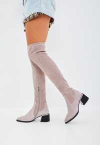 Cizme peste genunchi din suede gri deschis, cu fermoar pe lateral, vârf ascuțit și toc pătrat cu accent texturat negru.