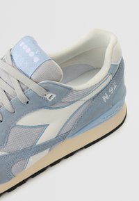 Light blue and gray sneaker featuring suede and mesh materials, with a white leather accent and smooth texture, designed with a padded tongue.