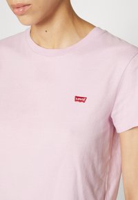 Világos rózsaszín pamut póló rövid ujjakkal. A bal mellkas területén található egy kis piros Levi's logó. Klasszikus kerek nyakkivágás.