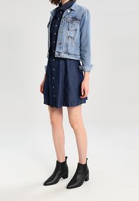 Ljusblå denimjacka över en mörk denimskjortklänning, tillsammans med svarta ankelboots. Funktioner inkluderar knappar, fickor och uppvikta ärmar.