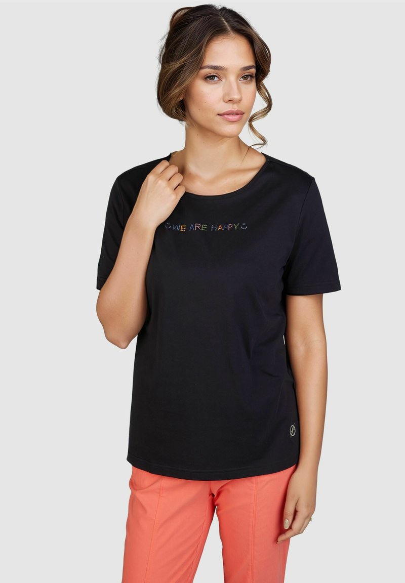 Schwarzes T-Shirt mit kurzen Ärmeln, Rundhalsausschnitt und buntem "WIR SIND GLÜCKLICH"-Text auf der Vorderseite. Kombiniert mit korallenfarbenen Hosen.