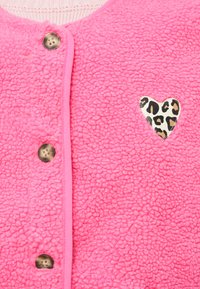 Ζακέτα από φλις σε έντονο ροζ χρώμα με απαλή υφή, διακοσμημένη με καρδιά σε σχέδιο λεοπάρ και στρογγυλά μεταλλικά κουμπιά κατά μήκος του μπροστινού μέρους.
