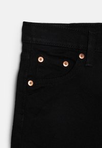 Vaqueros de denim negro con remaches de color cobre, un bolsillo delantero y una tela texturizada. Diseñados con un estilo clásico de cinco bolsillos.