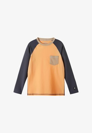 Koszulka raglan z długim rękawem, pomarańczowym korpusem, ciemnoszarymi rękawami, beżowym kołnierzem i kieszenią na piersi oraz logo na mankiecie lewego rękawa.