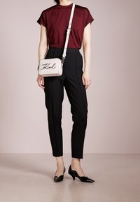 Burgundowy, paskowany top z krótkim rękawem, czarne zwężane spodnie oraz czarne lakierowane szpilki. Mała beżowa torebka na ramię z napisem "Karl" w kursywie.