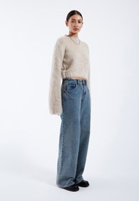 Beige fuzzy knit sweater with long sleeves, paired with high-waisted light blue wide-leg jeans and black slip-on shoes. Minimalist design.