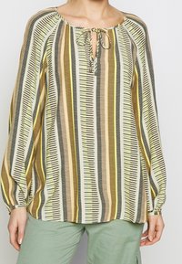 Blouse à rayures verticales jaunes, noires, roses et oliviers, avec un décolleté en forme de trou de serrure et de longues manches bouffantes. Tissu léger.