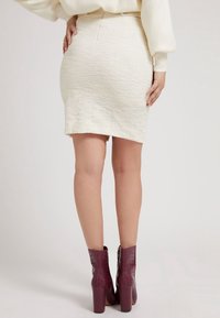 Bílá texturovaná tužková sukně s rovného lemu. Kombinována s vínovými koženými ankle boots s motivem krokodýlí kůže, které mají blokový podpatek a zipový uzávěr.