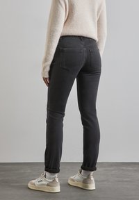 Svarta jeans med en figursydd design, med bakfickor och subtila sömnadsdetaljer, kombinerade med ljusa sneakers och uppvikta benslängder.