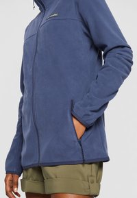Marine fleecejakke med glidelås foran, sidelommer og brodert logo. Har en glatt tekstur og en fitted design med lange ermer.