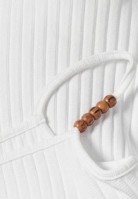 Tessuto bianco a coste con una tracolla arrotondata decorata con perline marroni. La texture è liscia con linee verticali.