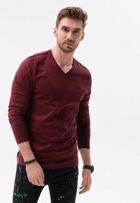 Vinröd långärmad V-ringad t-shirt i mjukt material, kombinerad med svarta jeans med färgstänk.