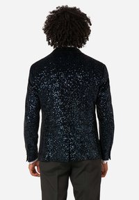 Tmavo modrý sako s flitrami a textúrovaným povrchom, s vykrojenými klopami a jedným rozventilovaním, skombinované s čiernymi nohavicami.