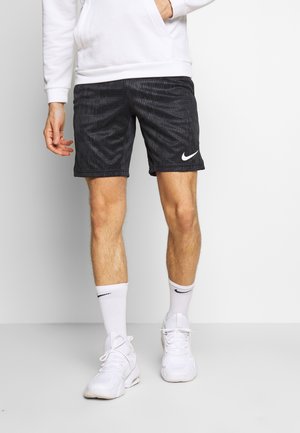 Czarne szorty w prążki z teksturowanej tkaniny, z białym logo Nike. Noszone z białymi butami sportowymi i skarpetkami, w komplecie z białą bluzą z kapturem.