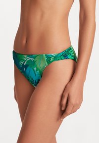 Bikini-bunn med et tropisk løvdesign i livlige nyanser av grønn og blå, laget av elastisk materiale med lavt liv. 
