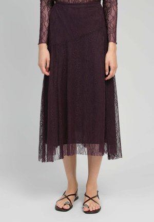 Jupe midi en dentelle de couleur violet profond avec des motifs floraux complexes, design en couches et un voile translucide ; accompagnée de sandales plates à lanières.