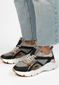 Sportieve sneakers in grijs, zwart en metallic goud. Voorzien van mesh stof, een gevoerd schouderdeel, witte veters en een dikke, witte zool.