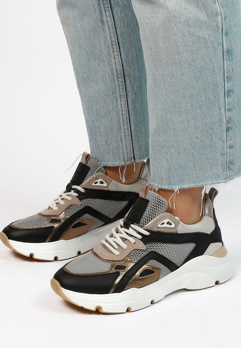 Sportieve sneakers in grijs, zwart en metallic goud. Voorzien van mesh stof, een gevoerd schouderdeel, witte veters en een dikke, witte zool.