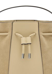 Beżowa skórzana torba tote o gładkim wykończeniu, z centralnym zapięciem na sznurek i metalicznymi akcentami na końcach.