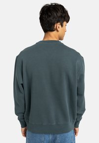 Sweatshirt verde scuro con colletto a giro e polsini a coste, caratterizzato da una vestibilità rilassata e una texture morbida, mostrato da dietro.