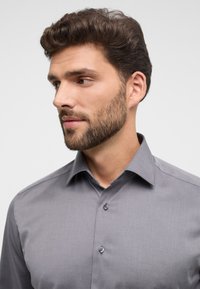 Graues Button-Down-Hemd mit einem Kentkragen, das über eine glatte Textur und einen subtile Glanz verfügt, akzentuiert durch dunkle, runde Knöpfe.