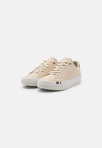 Beige läder sneakers med rund tå, platta snören, vit gummisula och subtila randiga accenter i blått, vitt och rött nära hälen.