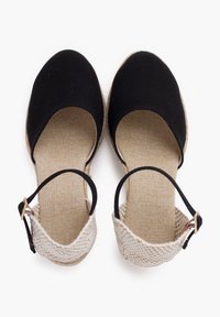 Black canvas espadrilles with a woven beige ankle strap and textured beige insole. The sole is slightly raised with a natural jute finish.
