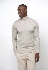 Beige Rollkragenpullover, taillierte Passform, gerippte Bündchen und Saum, glatte Textur. Kombiniert mit hellbeigen Cordhosen.