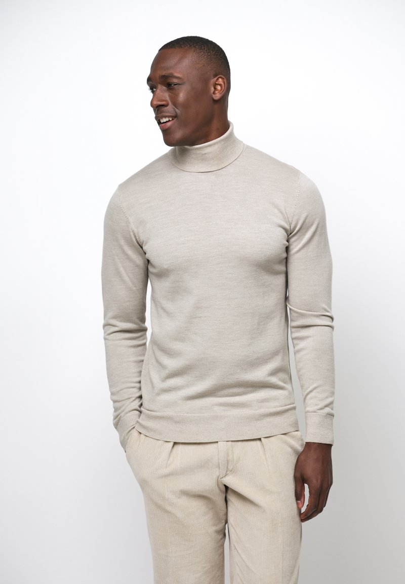 Beige Rollkragenpullover, taillierte Passform, gerippte Bündchen und Saum, glatte Textur. Kombiniert mit hellbeigen Cordhosen.