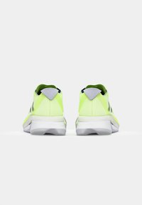 Lys gule atletiske sko med et slankt design, vist fra bagsiden, med en grå accent på hælen, mod en enkel baggrund.