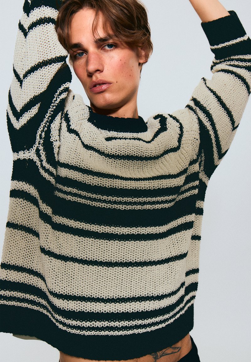 Maglione con vestibilità ampia, caratterizzato da righe orizzontali nere e crema. Realizzato in tessuto lavorato a maglia con texture visibile e morbida caduta.