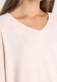 Ljusrosa tröja med V-ringning, mjukt texturerat tyg och löst sittande ärmar.