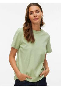 Lysegrøn kortærmet t-shirt lavet af blødt materiale med rund halsudskæring. Modellen har hænderne i lommerne, kombineret med mørke jeans.