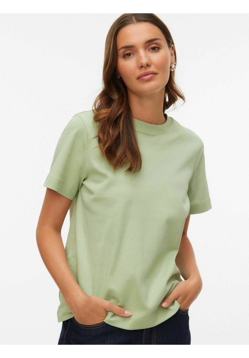 Lysegrøn kortærmet t-shirt lavet af blødt materiale med rund halsudskæring. Modellen har hænderne i lommerne, kombineret med mørke jeans.