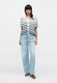 Πλεκτή ζακέτα με μπλε και λευκές ρίγες, κούμπωμα με κουμπιά, σε συνδυασμό με ανοιχτό μπλε τζιν παντελόνι φαρδιάς γραμμής και παπούτσια με λεοπαρ μοτίβο.