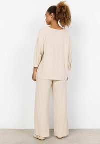 Beige ribbad stickad oversize topp med trekvartslånga �ärmar och matchande vida byxor. Slät textur med subtila vertikala linjer.