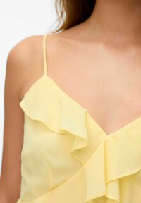 Geel blouse met dunne spaghetti banden, voorzien van gerimpelde lagen langs de halslijn. Lichtgewicht, vloeiend materiaal met een zachte textuur.