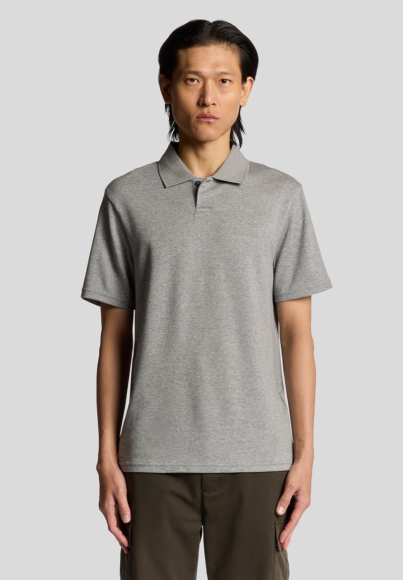 Polo shirt gris en mélange de coton, avec des manches courtes, un col classique et une patte de boutonnage à deux boutons. Le modèle porte un pantalon cargo olive.
