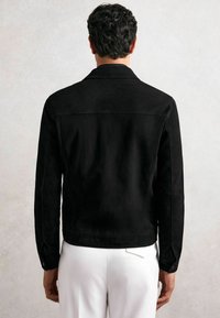 Melna zamšādas jaka ar apkakli, garām piedurknēm un redzamām šuvju detaļām. Aizmugurei ir gluda tekstūra un pielāgota forma.