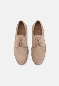 Zapatos de ante beige con diseño de cordones, acentos cosidos y punta redonda. El interior presenta el logo de la marca.