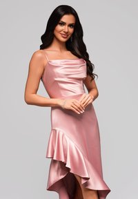 Różowa satynowa sukienka z drapowanym gorsetem i asymetrycznym hemline'em z falbaniastym akcentem. Ramiączka typu spaghetti i gładka tekstura.