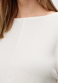 Witte geribbelde top met een lichte boothals. Materiaal lijkt zacht en gestructureerd met subtiele naden langs de schouder en het lichaam.