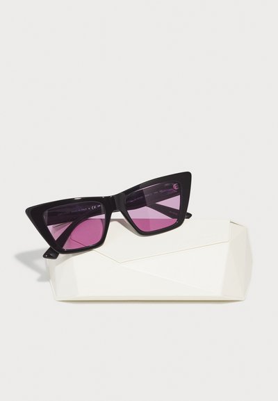 Ochelari de soare negri în stil cat-eye cu lentile de un purpuriu închis, așezați pe un etui geometric alb, evidențiind linii ascuțite și un finisaj lucios.