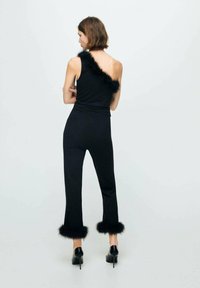 Ensemble en tricot noir avec un haut asymétrique ornée de fausse fourrure noire sur une épaule et sur les ourlets des pantalons. Design ajusté avec des jambes larges.