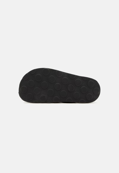 Semelle de chaussure noire avec de grands motifs circulaires antidérapants répartis uniformément sur la partie inférieure sur un fond clair uni.