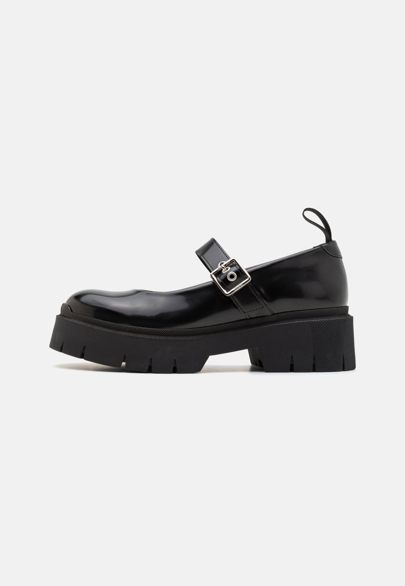 Chaussure Mary Jane noire à semelle épaisse, finition brillante, bride avec boucle carrée argentée et languette de tirage au talon sur fond uni.