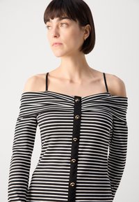 Robe noire et blanche à rayures, décolletée, avec un devant à boutons, présentant des détails de boutons dorés et une coupe ajustée.