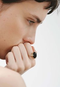 Anillo de oro con una gran piedra negra ovalada con cuatro engastes en forma de garra y pequeños acentos de diamante, llevado en el dedo de una persona.